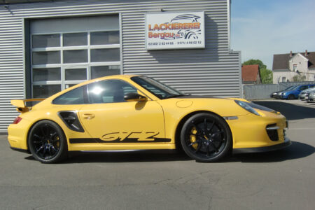 Gelber Porsche GT2 mit schwarzem Schriftzug vor der Lackiererei Bergau geparkt.